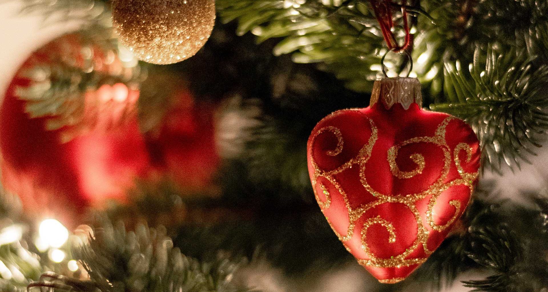 Close up image of Christmas tree with red, heart-shaped ornament in foreground