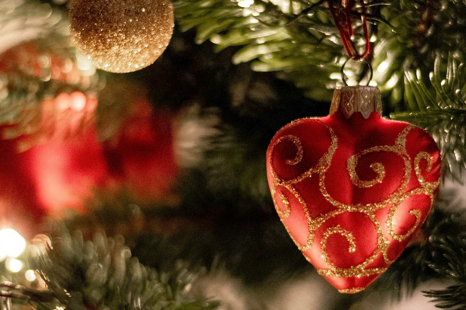 Close up image of Christmas tree with red, heart-shaped ornament in foreground