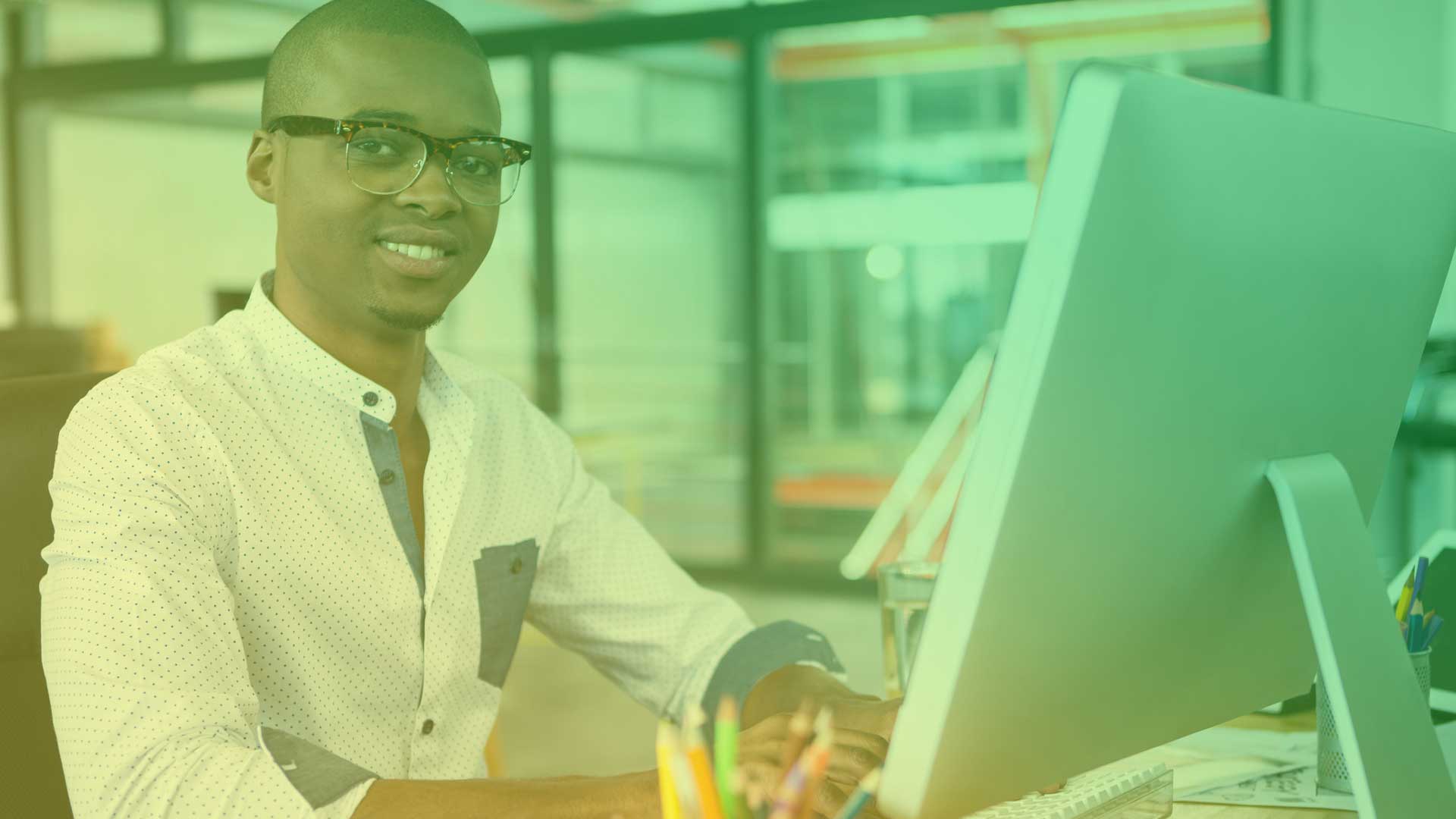 Young bespectacled African man smiling in font of desktop computer