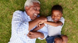 Old man and young boy lying on grass while playing