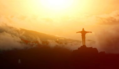 Picture of a person with open arms standing on a high area overlooking an expansive, sunlit view. | Image: Freepik