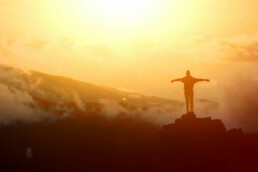 Picture of a person with open arms standing on a high area overlooking an expansive, sunlit view. | Image: Freepik