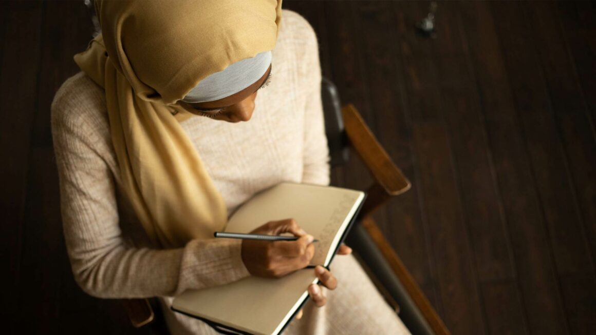 A woman wearing a head covering while writing on her notebook. Aerial View.